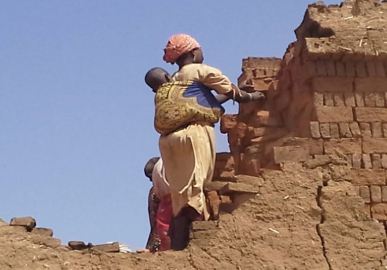 A woman working at a brick kiln while carrying her child at an IDP Camp near El-Fashier, Sudan