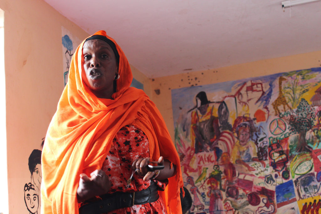 Woman speaking at a forum on Reducing Inter-ethnic Violence through Dialogue in Kenya with a wall of illustrations behind her.