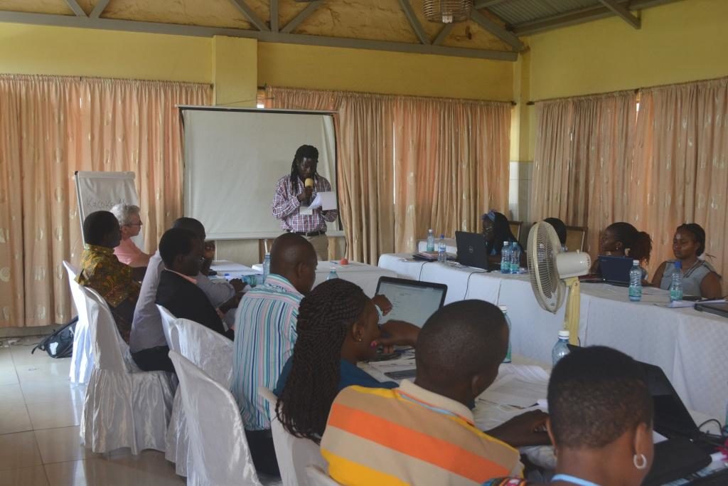 APN Alumnus Fredrick Ogenga at APN-sponsored Peace Journalism Workshop in Rongo, Kenya. Dr. Ogenga is standing and speaking in front of participants seated at horseshoe shaped conference table.